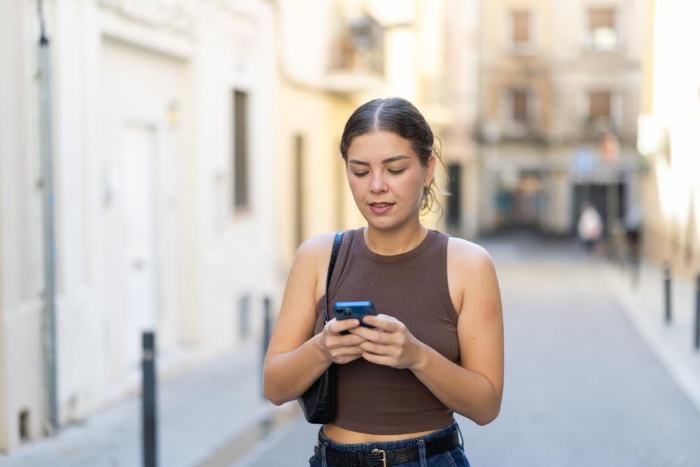 Young woman looking at smartphone while walking along street