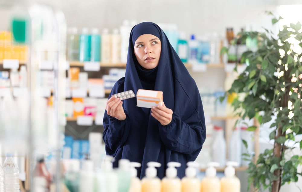Young Muslim woman customer choosing pills in box in drugstore