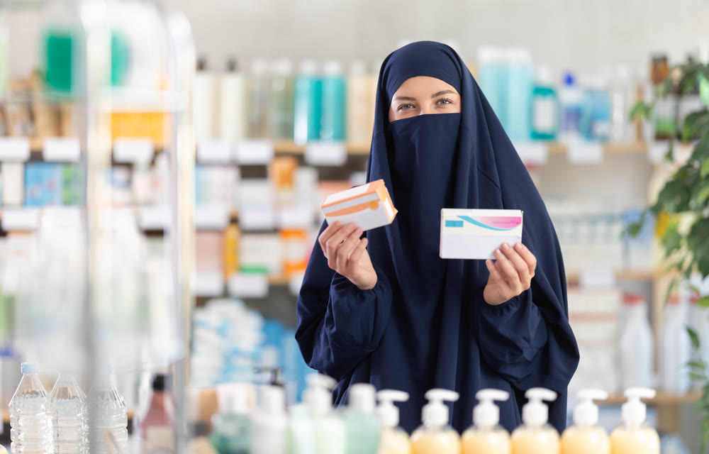 Woman in navy blue niqab checking label of prescribed medicine at pharmacy