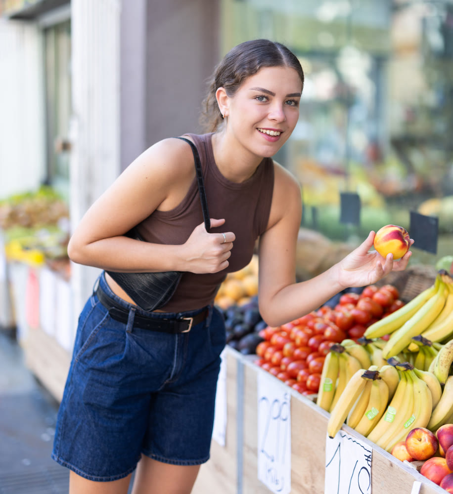 Girl is walking around street market or fair, choosing nectarine goods