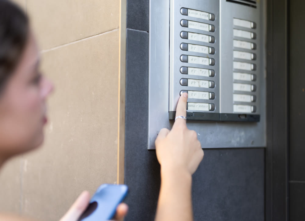 Girl with phone standing at entrance of building, ringing intercom