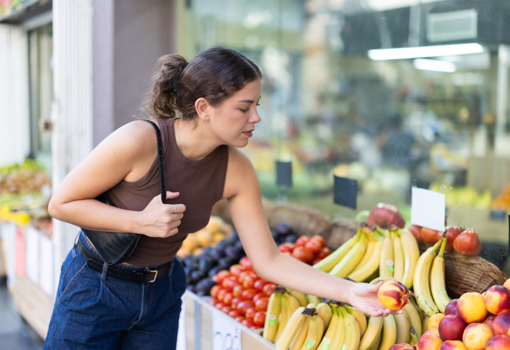 Girl is walking around street market or fair, choosing nectarine goods