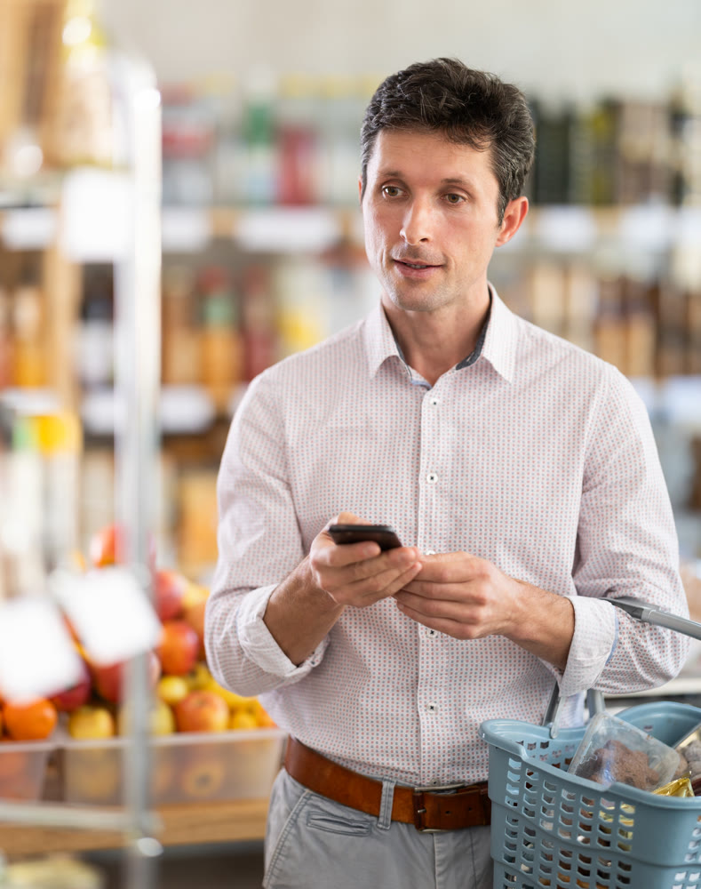 In store, man looks at phone screen, scrolls page, searches phones notes for shopping list