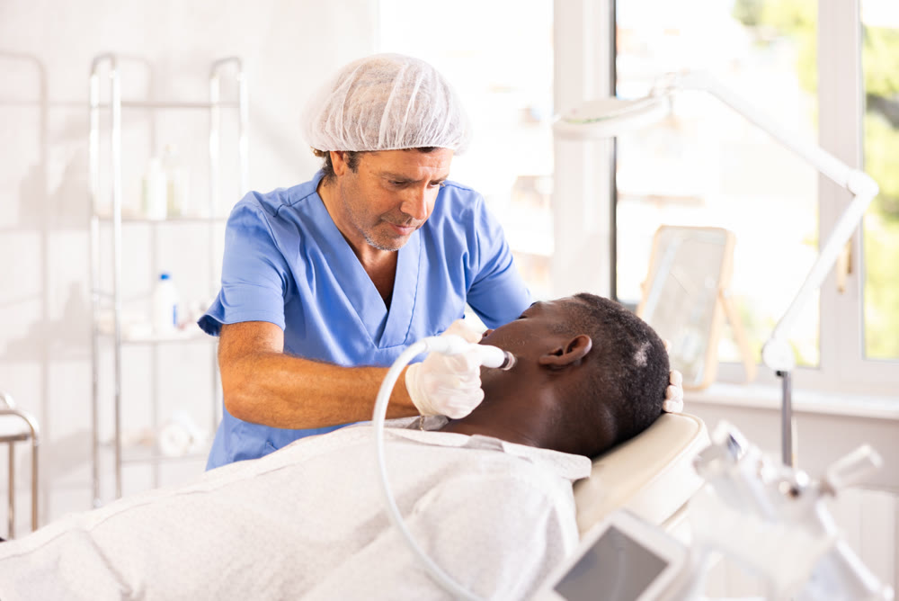 Cosmetologist performing facial procedure using ion bubble attachment on african american client