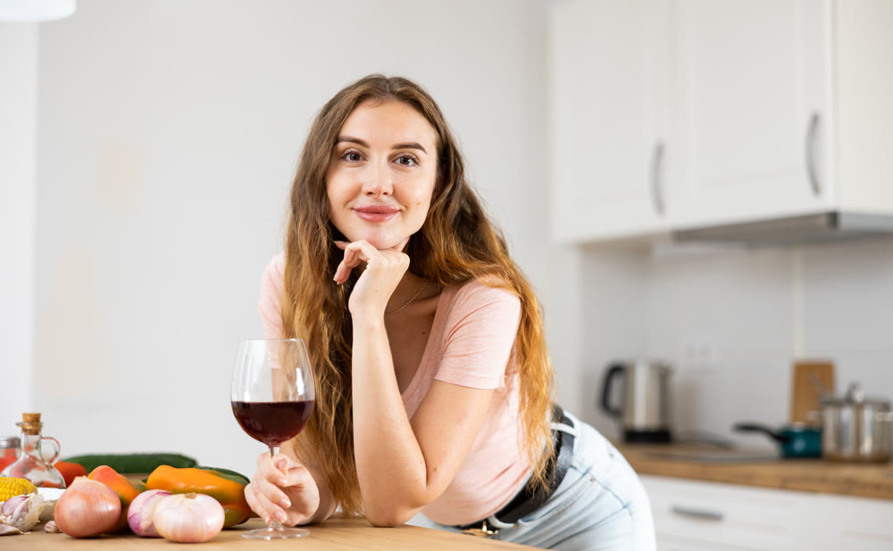 Portrait of satisfied woman with glass of red wine in modern kitchen