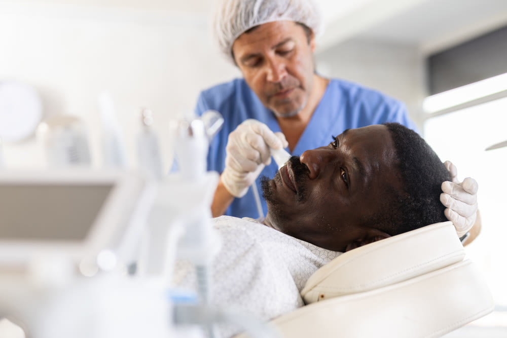 Male specialist uses ultrasonic import nozzle to care African man client face skin