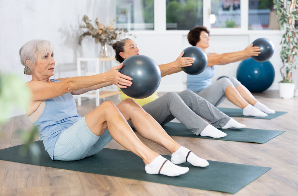 Elderly women perform softball exercises sitting on floor, workout for beautiful figure, toned body