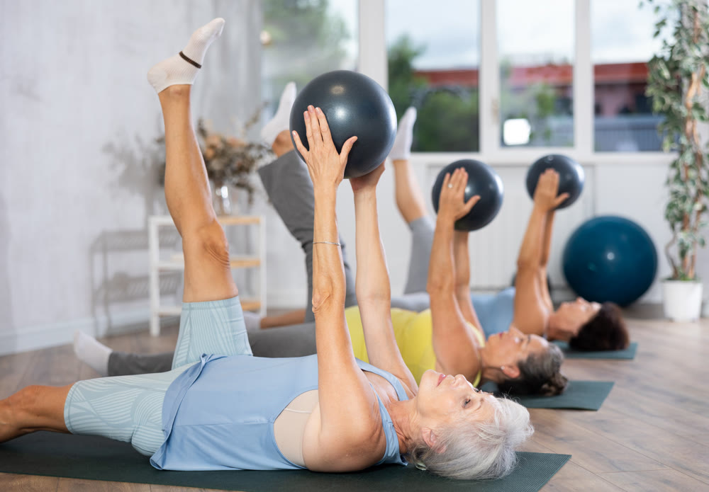 Elderly women perform softball exercises lying on floor, workout for beautiful figure, toned body