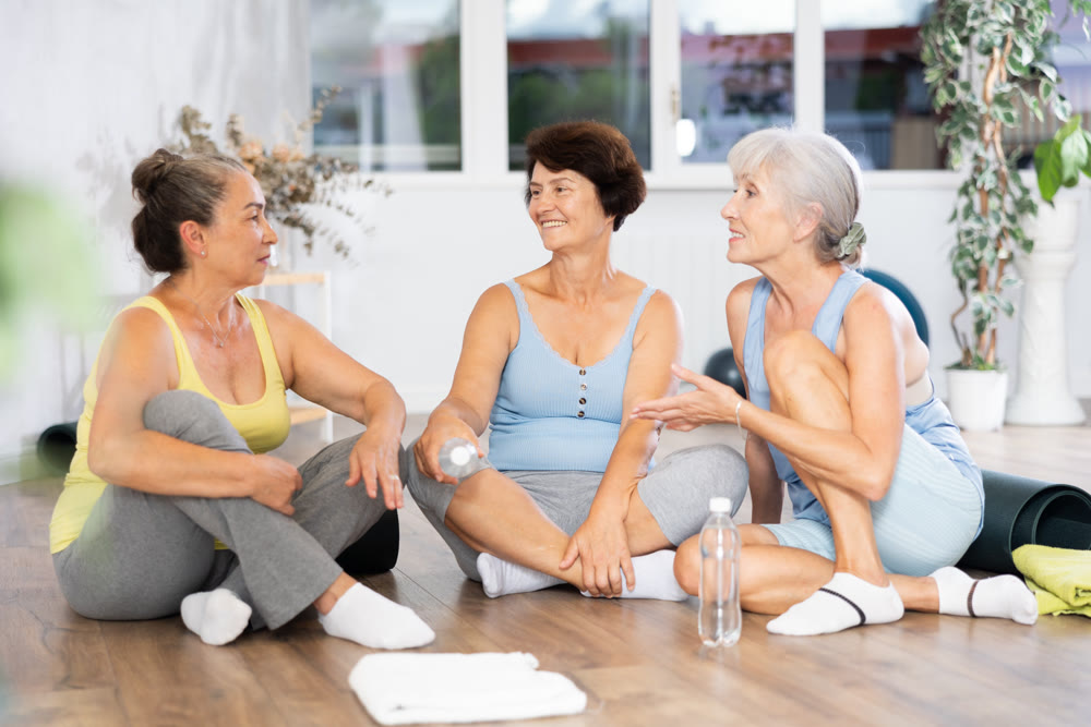 Mature women talking to each other sitting on the floor in fitness studio