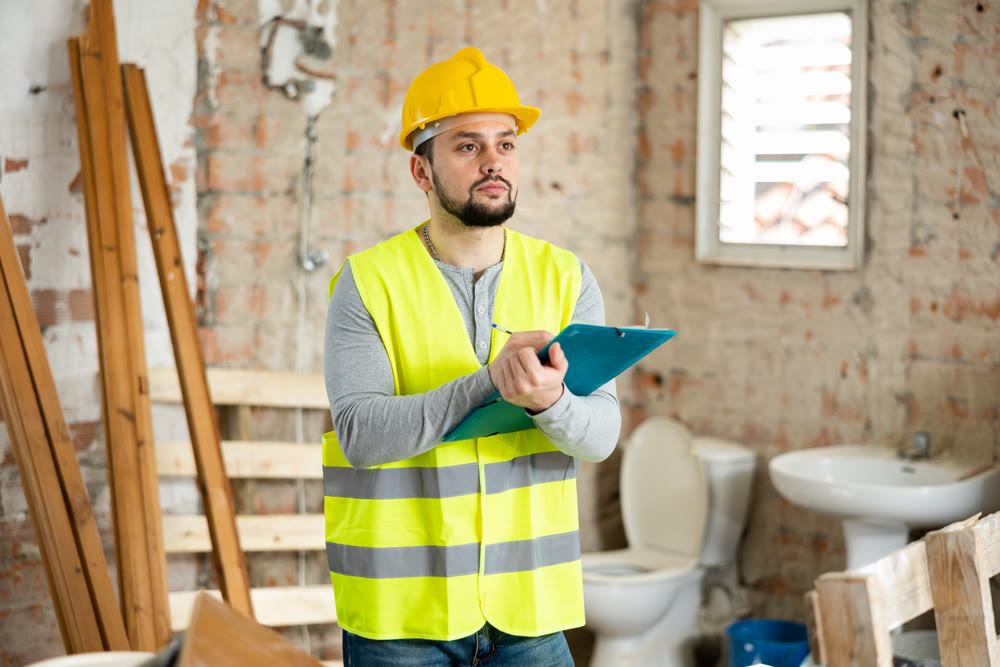 Man in in a yellow vest and hardhat checks the completed construction work on drawing