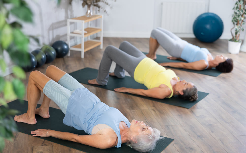 Old woman practicing bridge pose of yoga in training room during fitness classes
