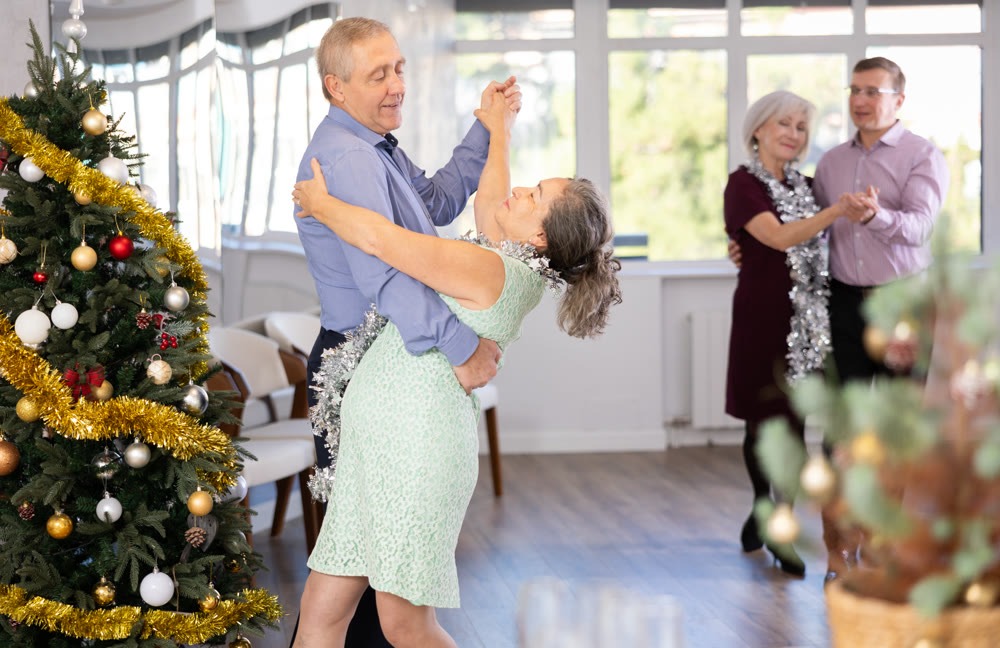 Positive senior man dancing playful Latin dance bachata with female partner during celebration Christmas and New Year in choreography studio. Active lifestyle of older generation
