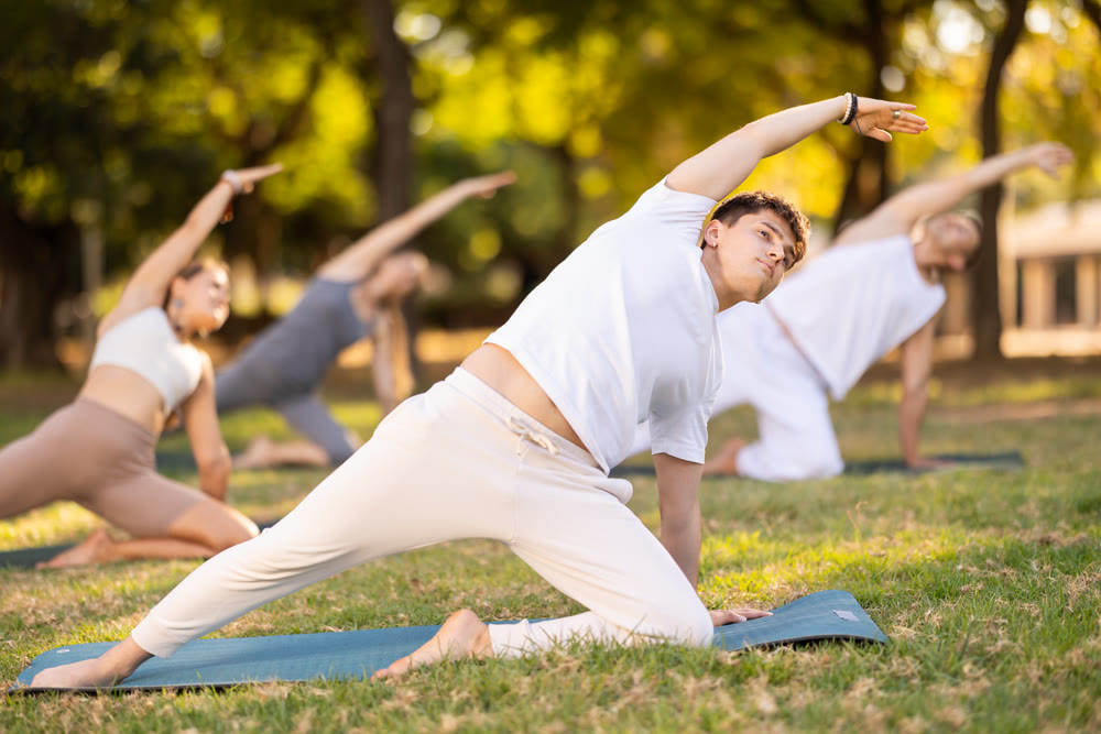Guy doing Reverse Gate Pose during group yoga in park