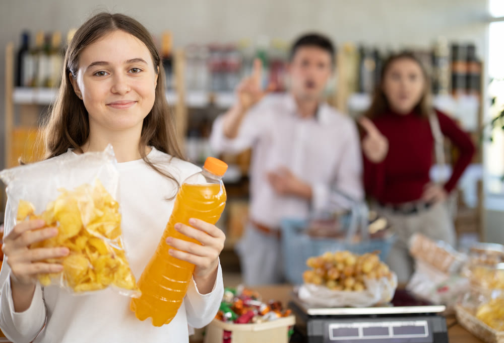 Teenage girl holding chips and juice in grocery store