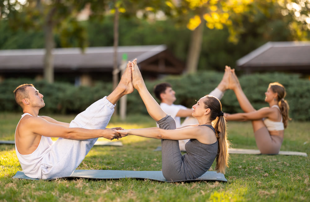 Young couple performing partner Boat pose during outdoor yoga class