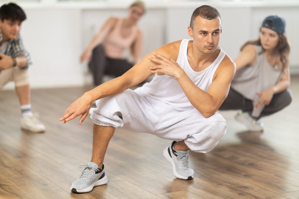 Teacher and her students squatting down and perform hip hop dance