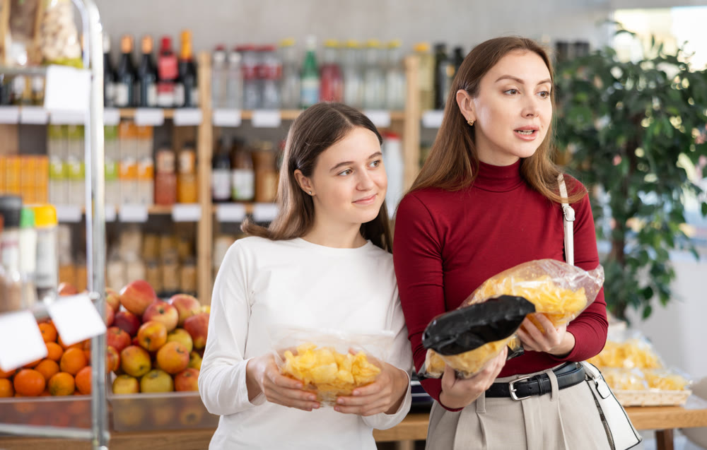 Teenage girl and her mother choosing chips in grocery store