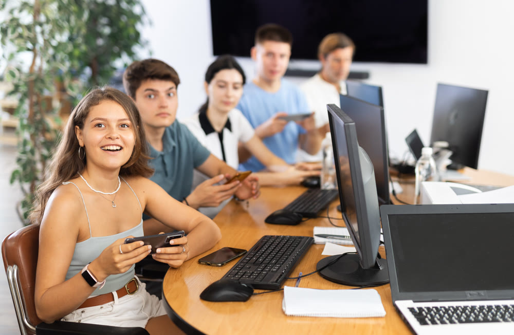 At computer class, young girl student sits with mobile phone and listens admiringly to teacher