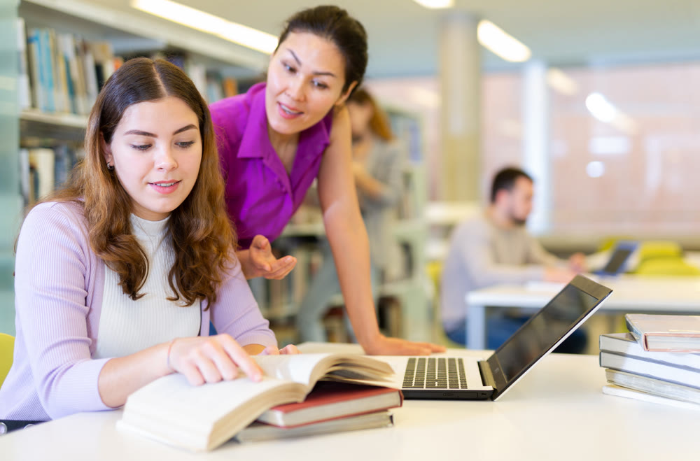 Two female friends studying together at library
