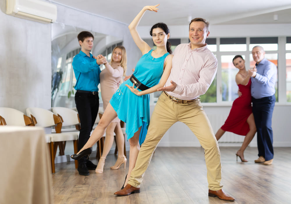 Men and women in festive clothes practicing tango dances in ballroom