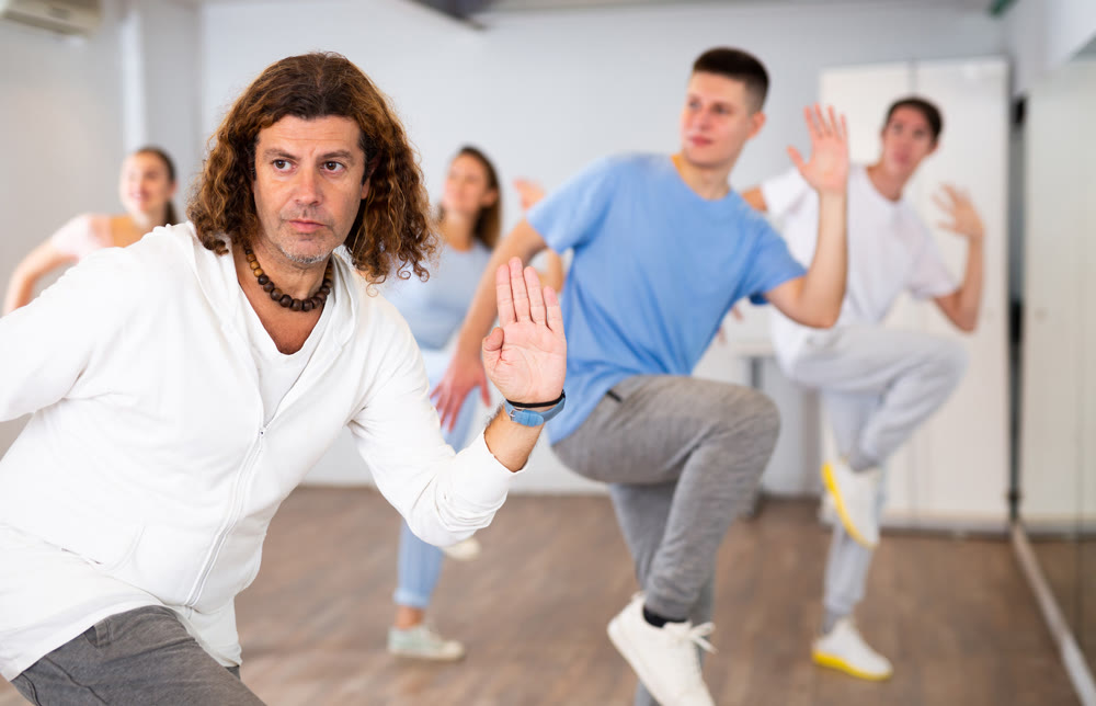 Active positive men and women performing dance elements during training together in modern fitness gym