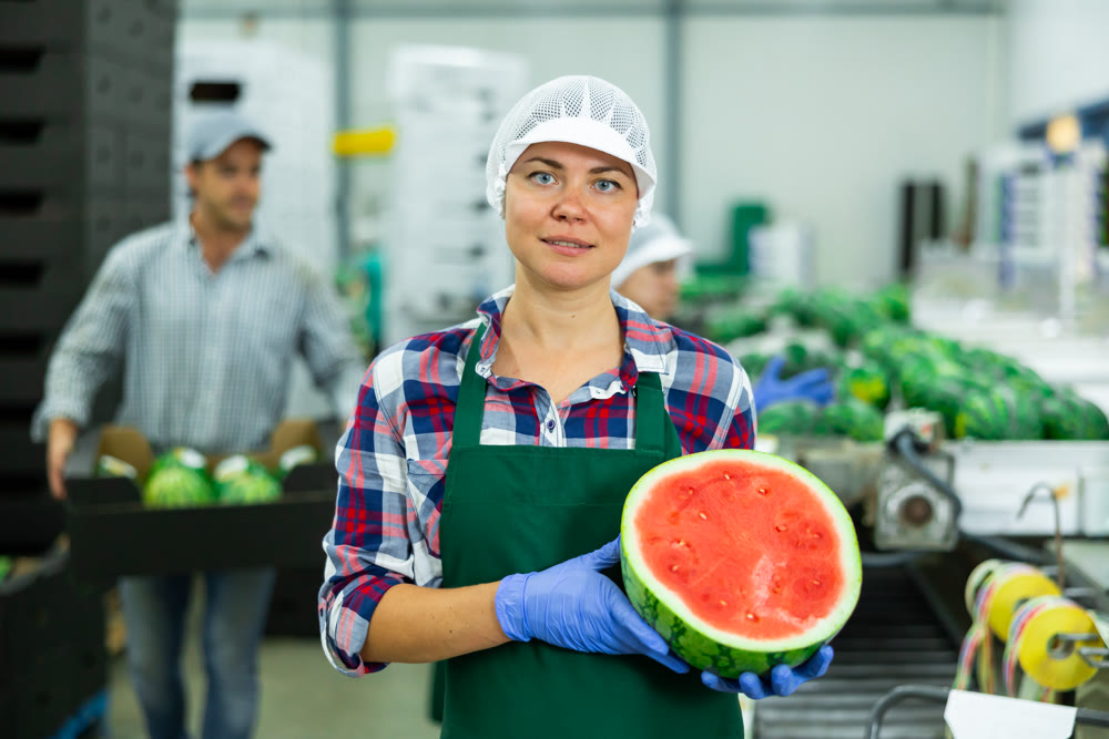 Happy woman fruit processing factory worker holding half of watermelon