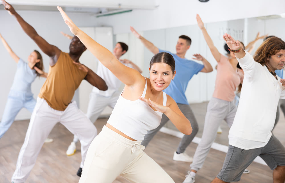 Joyful flexible multiethnic men and women exercising active moves with group of people in dance center