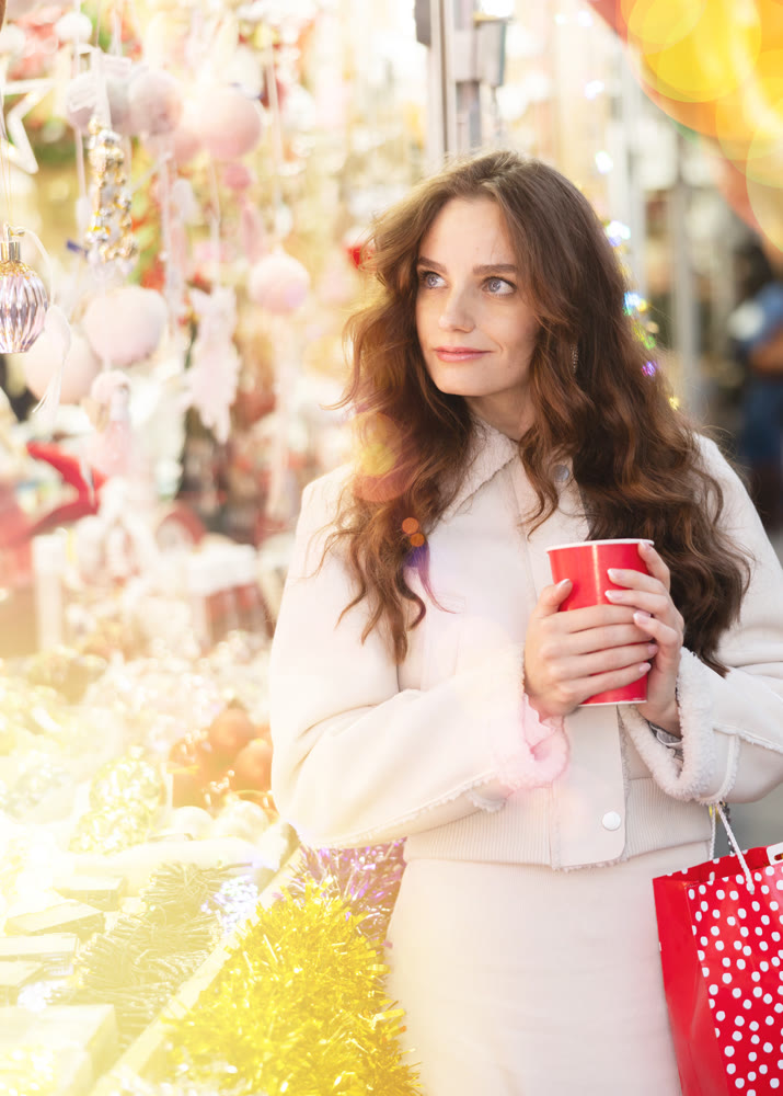 Smiling woman walking through Christmas street market with warm beverage in paper cup