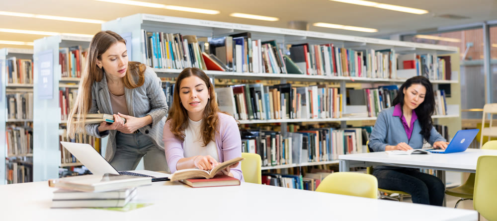Two female students studying in library with books and laptop