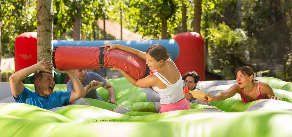 Cheerful girl fighting off friends with inflatable log while guarding toy chickens