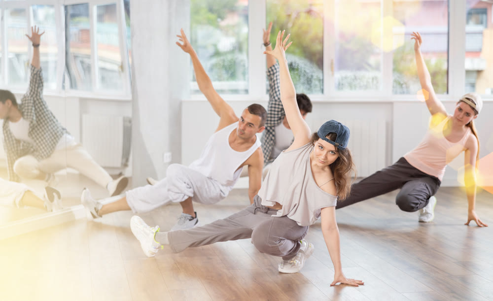 Girl and her students perform hip hop dance on one bent leg, movement in horizontal plane near floor
