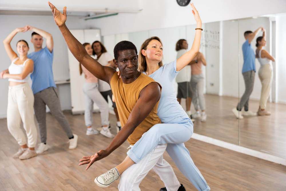 Joyful young adult couples learning passionate pair dancing during practicing in choreography class