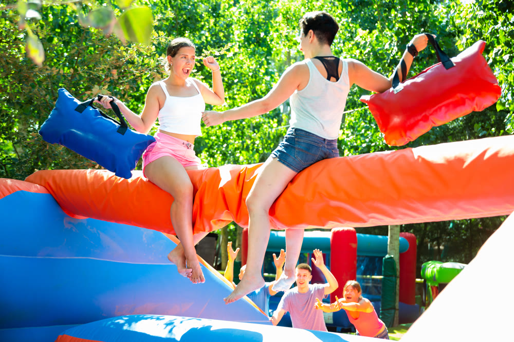 Happy girl funny pillow fighting on inflatable log with female friend
