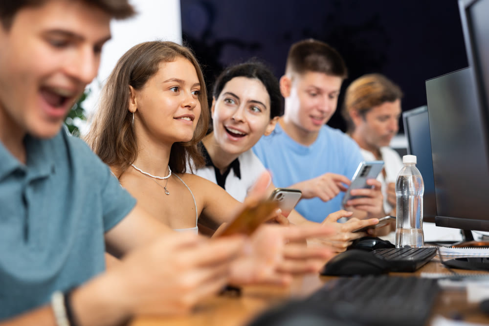 Cheerful young female student using mobile phone in computer workshop