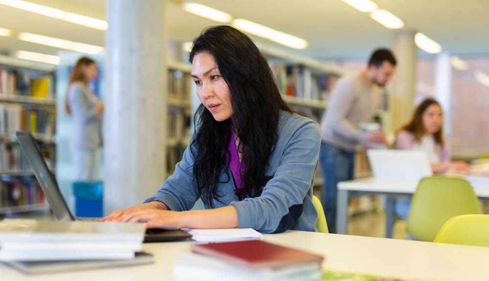 Asian woman working with laptop and books on science project in library