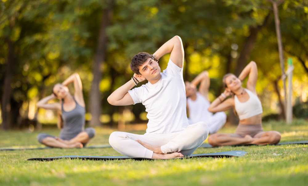 Yoga lesson visitors with guy coach perform padmasana in park