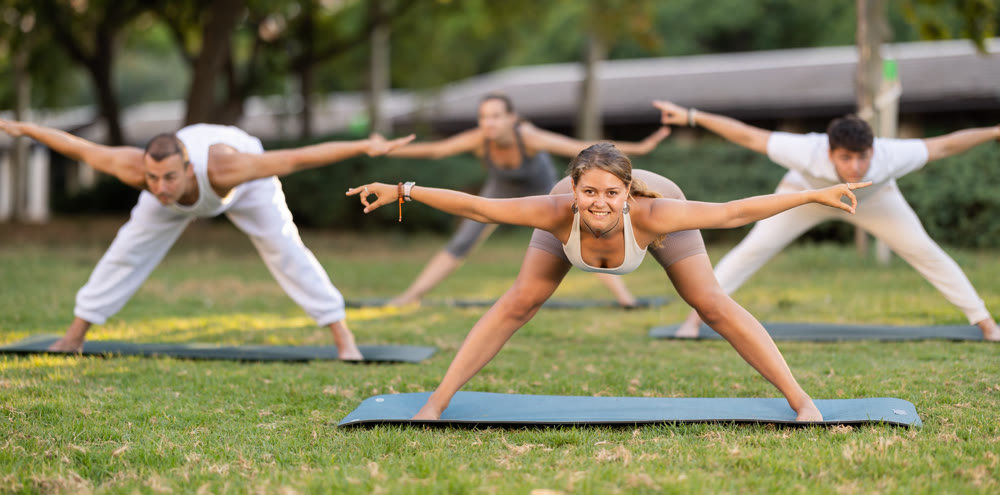 Yoga lesson visitors with coach perform Prasarita Padottanasana in park