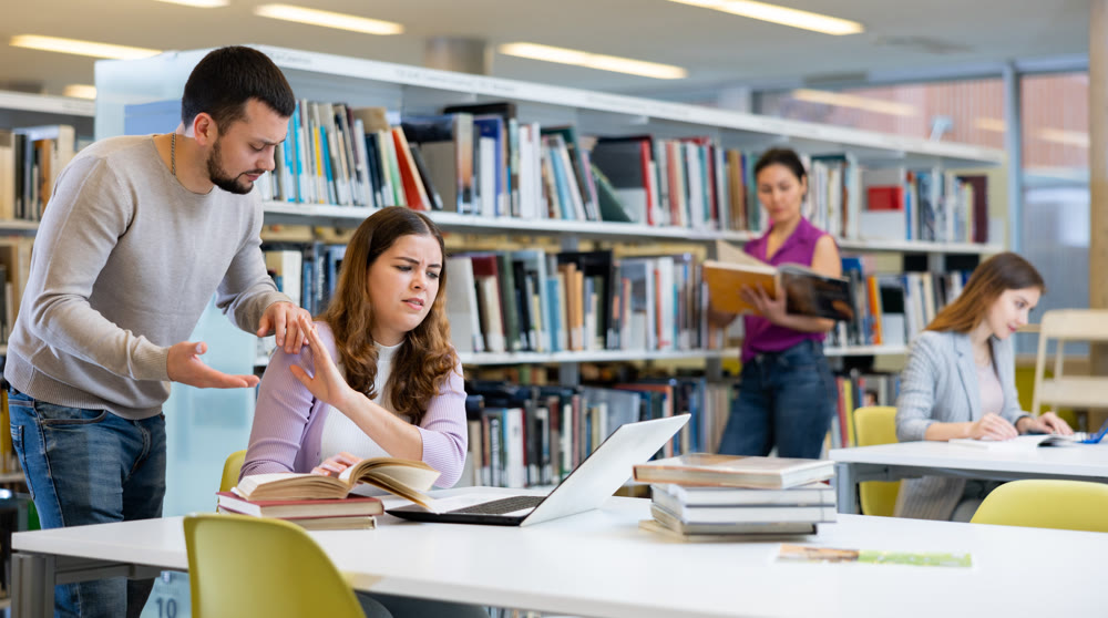 Students in the library are engaged on a laptop, discussing something