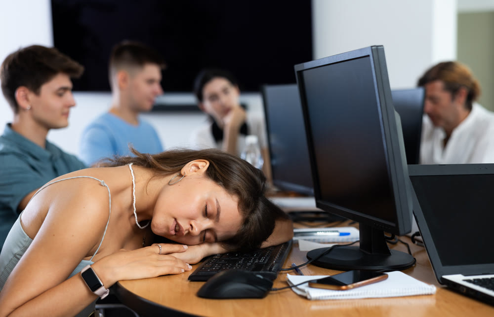 Exhausted young female student sleeping at table in computer classroom