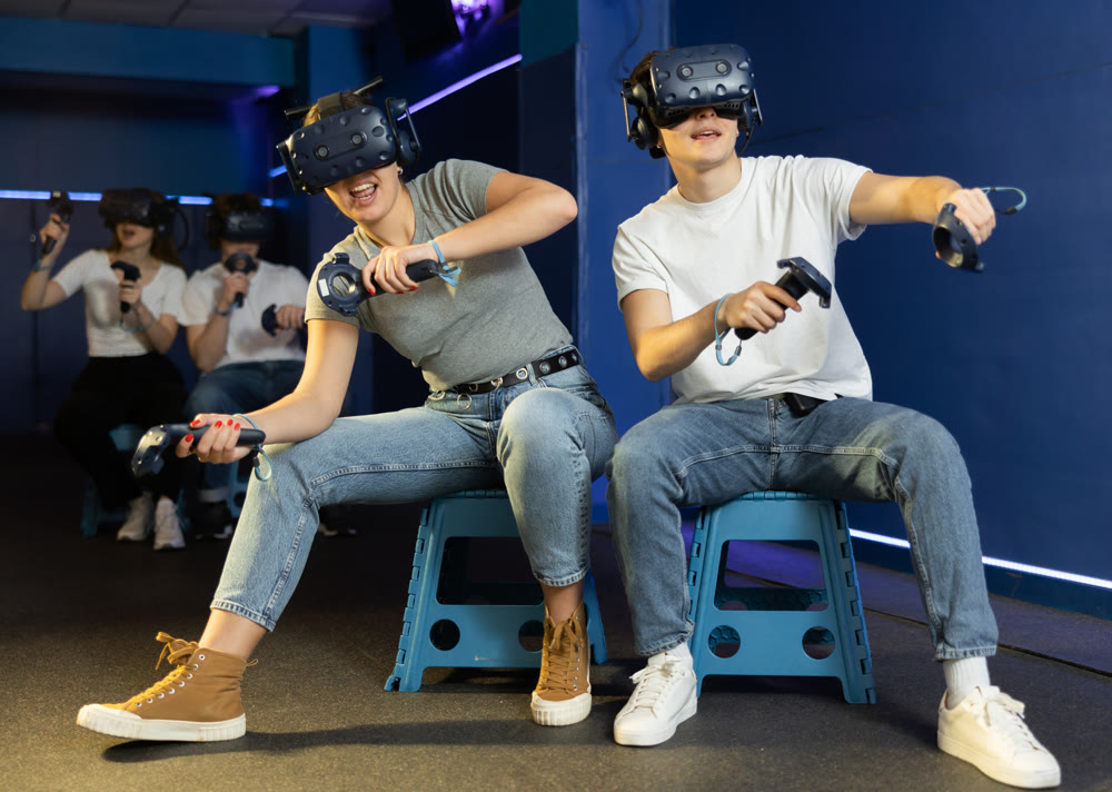 Emotional young couple with VR headsets and joysticks immersed in game