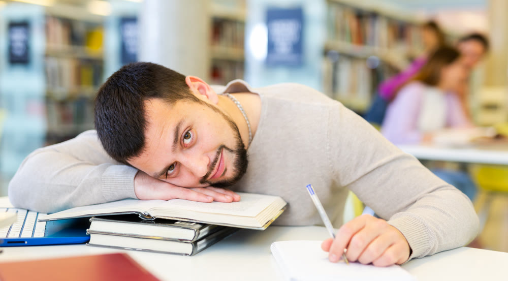 Lazy young bearded student lying on books at table in library
