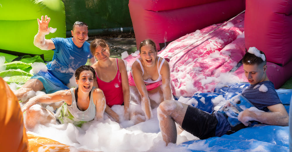 Cheerful friends picking up balls in inflatable pool full of foam