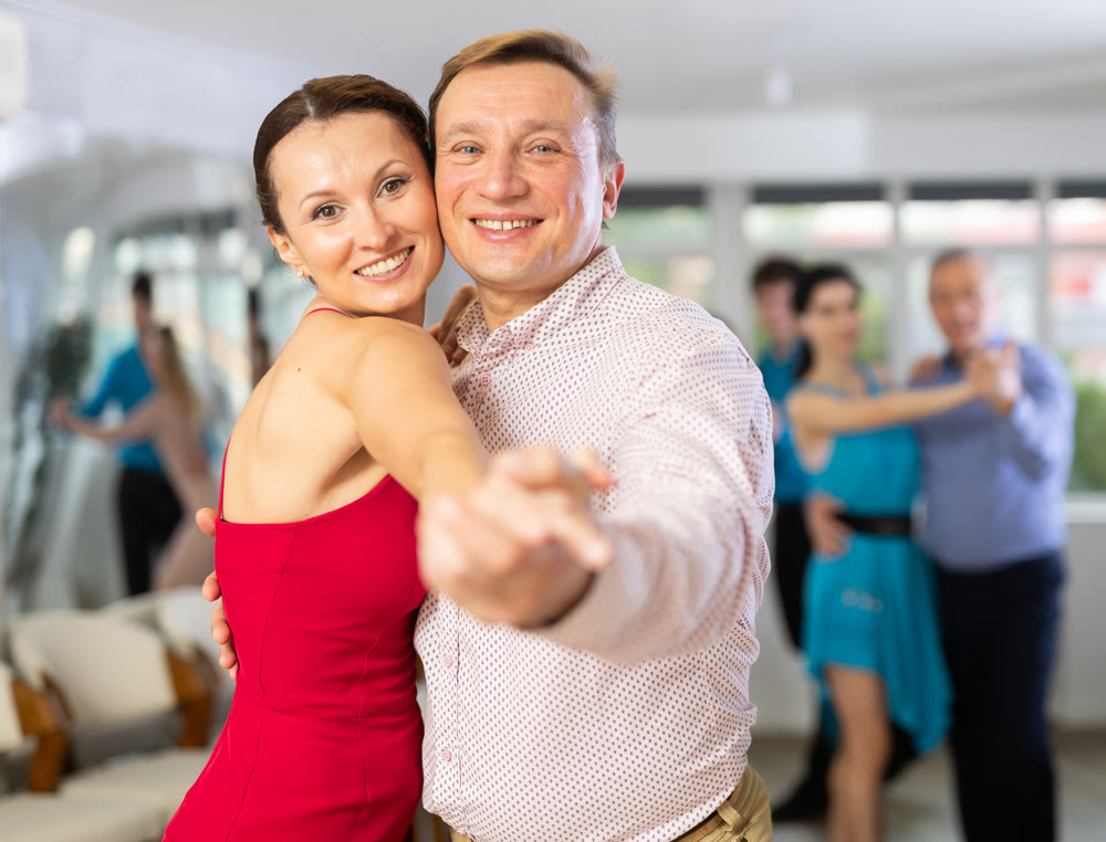 Happy people of different ages dancing tango in pairs in dance hall