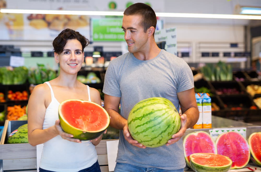 Positive couple with watermelons in supermarket