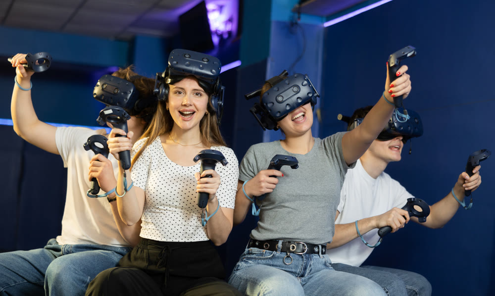 Female student with vr headset on forehead and analog stick sits next to gamer friends