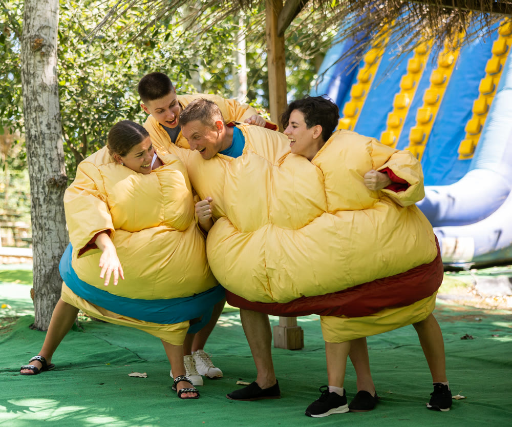 Two couples in inflatable double sumo suits fighting in outdoor playground