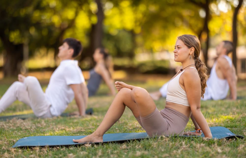 Yoga lesson visitors with girl coach perform halasana in park