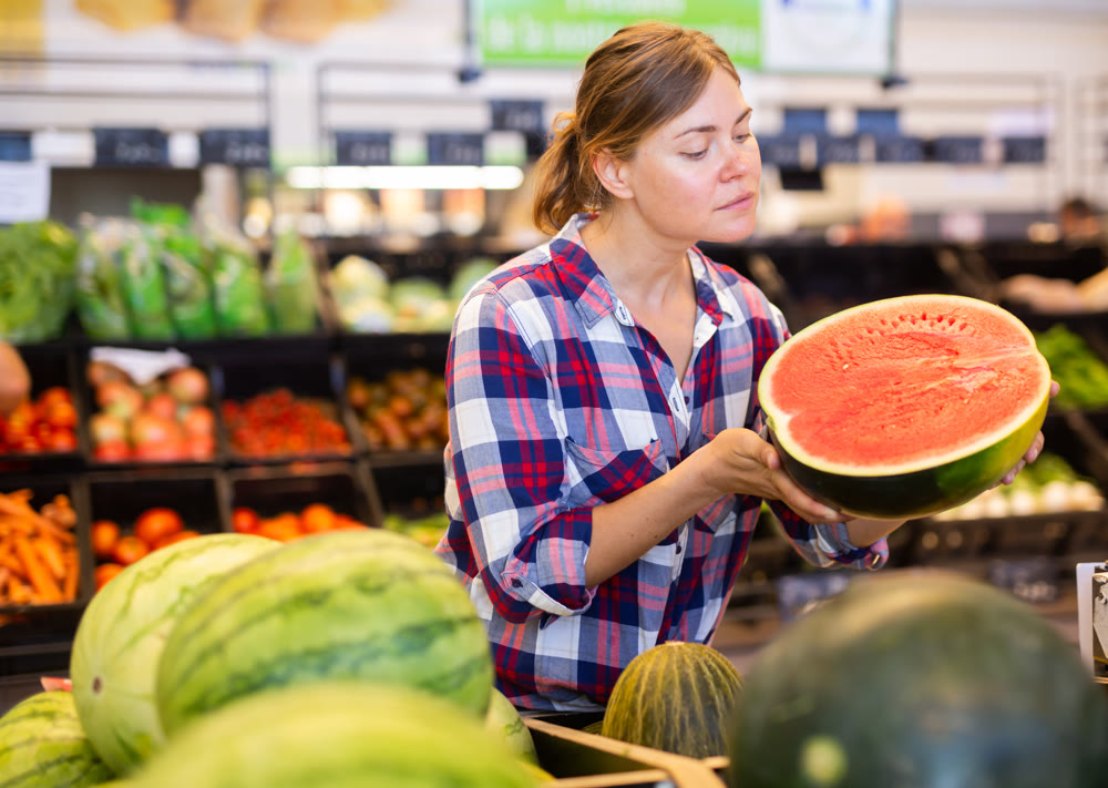 Positive woman customer choosing ripe watermelon in supermarket