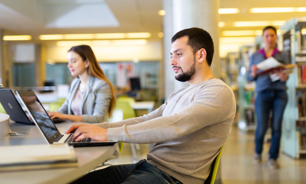 Guy student studies in the library on a laptop