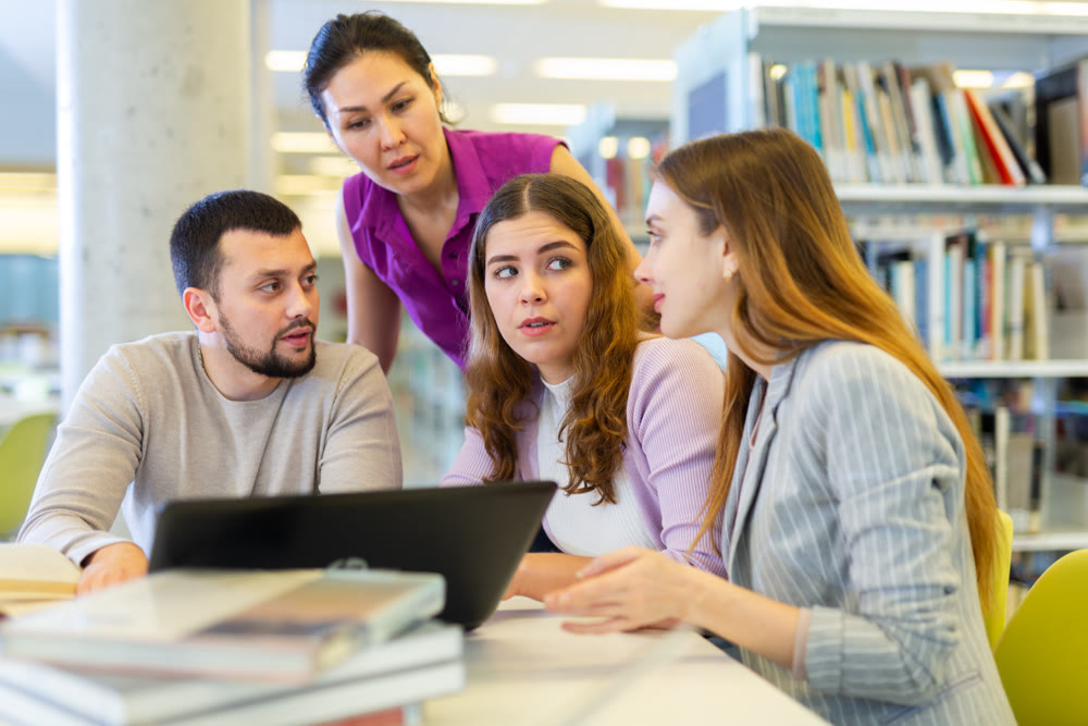 Group of students in the library is preparing for classes on a laptop